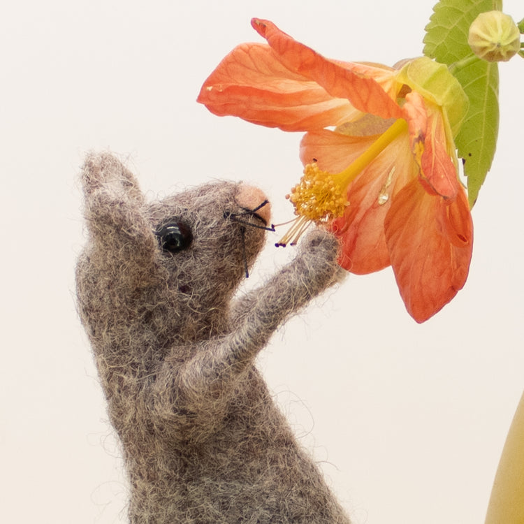 cute needle felted mouse reaching into a flower to smell its scent 